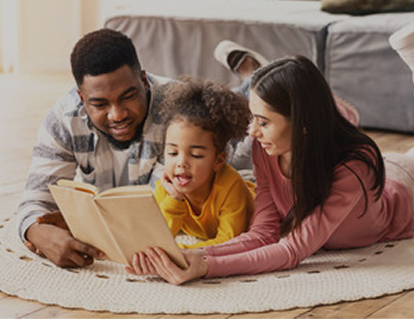 Deux parents avec leur enfant qui lisent un livre couché sur un tapis